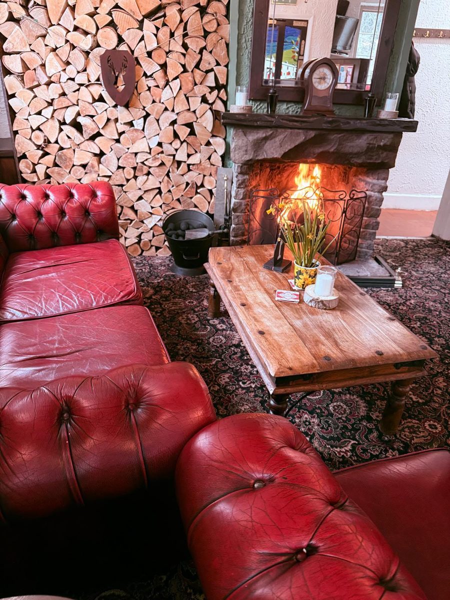The open fire at The Poachers Inn, lit, with red leather armchairs and a stacked log wall