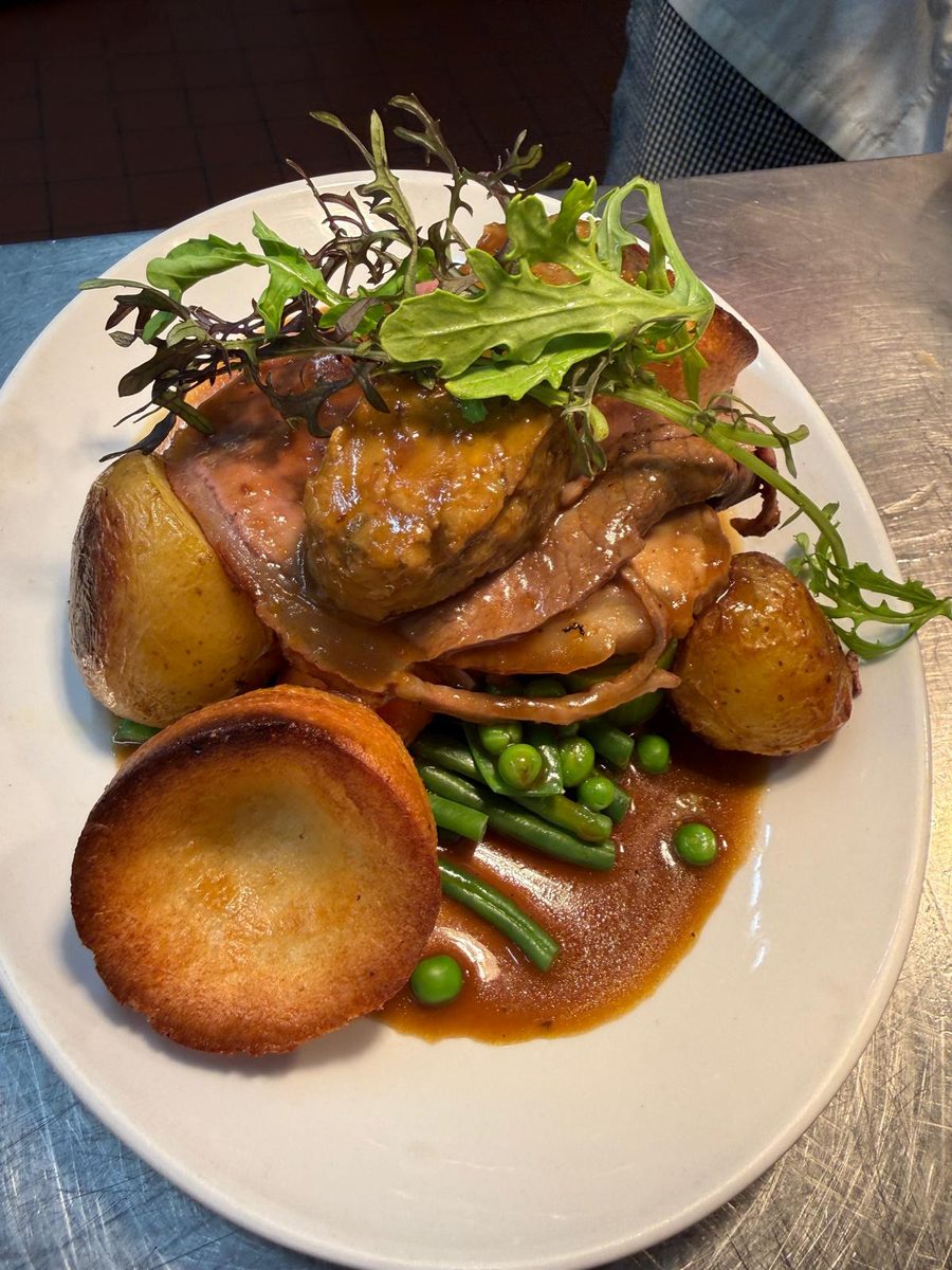 A roast dinner at The Poachers Inn: sliced roast meats with a Yorkshire pudding, roast potatoes, green beans and peas, and plenty of gravy